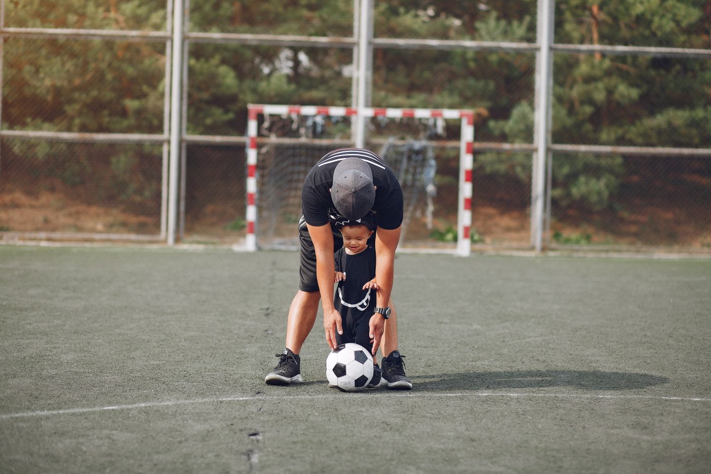Vater begleitet seinen kleinen Sohn mit Ball auf dem Fußballplatz – Beratung für Eltern und Familien
